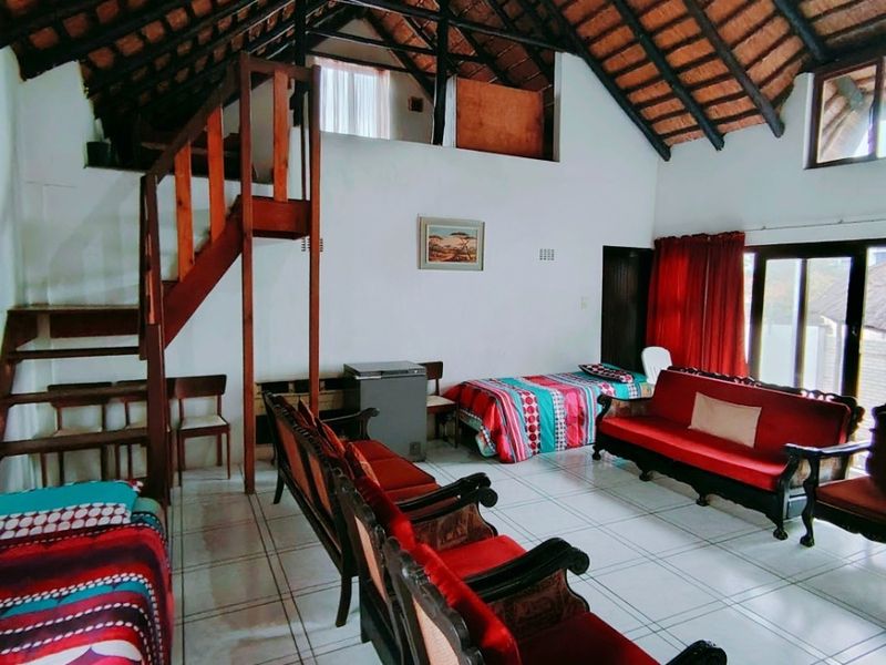 Spacious living area featuring high vaulted ceilings with exposed timber trusses, tiled flooring, a mezzanine level, and direct access to the outdoors via sliding doors.