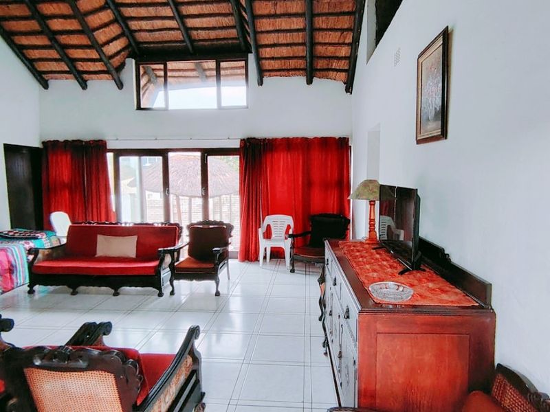 Spacious living area featuring a high vaulted ceiling with exposed timber rafters, thatched roof finish, tiled flooring, and large sliding glass doors.