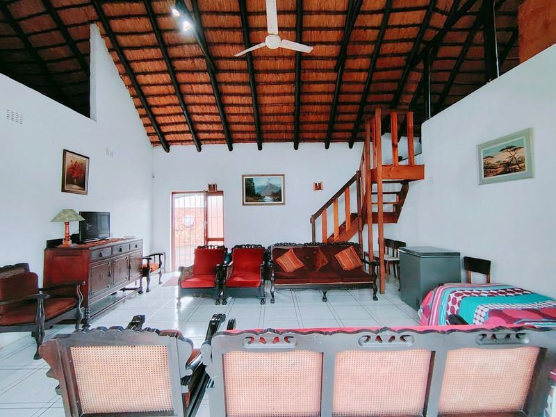 Spacious living area featuring a high vaulted thatched ceiling with exposed timber rafters, tiled flooring, and a wooden staircase leading to an upper level.