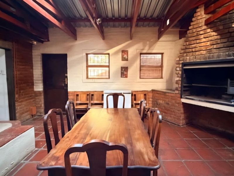 Covered outdoor patio featuring exposed timber rafters, terracotta flooring, and a built-in brick braai, ideal for entertaining.