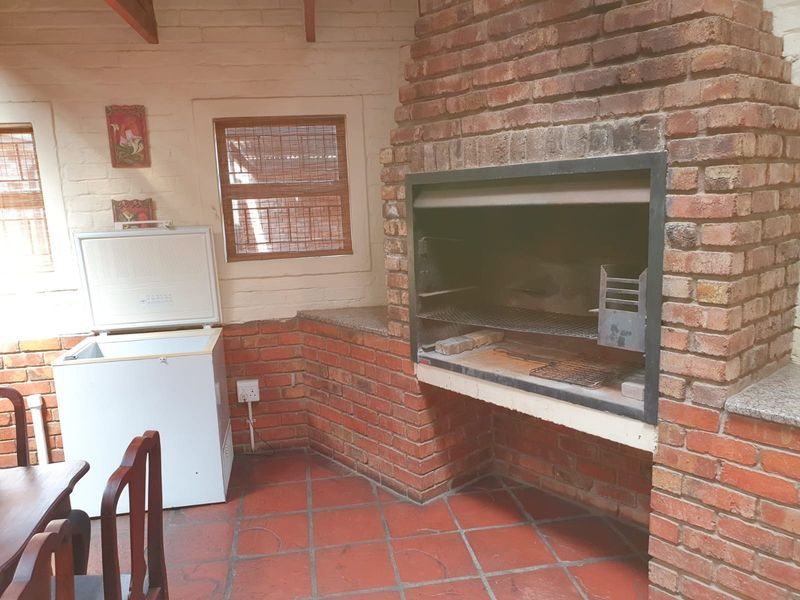 Covered patio area featuring a built-in brick braai, terracotta flooring, and exposed brick walls, providing a rustic outdoor entertainment space.