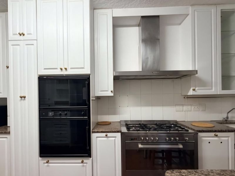 A functional kitchen featuring white cabinetry, granite countertops, a built-in oven, and a stainless steel gas cooktop with an extractor fan.
