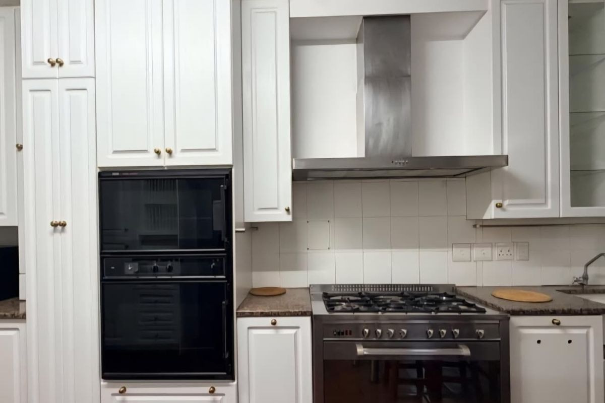 A functional kitchen featuring white cabinetry, granite countertops, a built-in oven, and a stainless steel gas cooktop with an extractor fan.