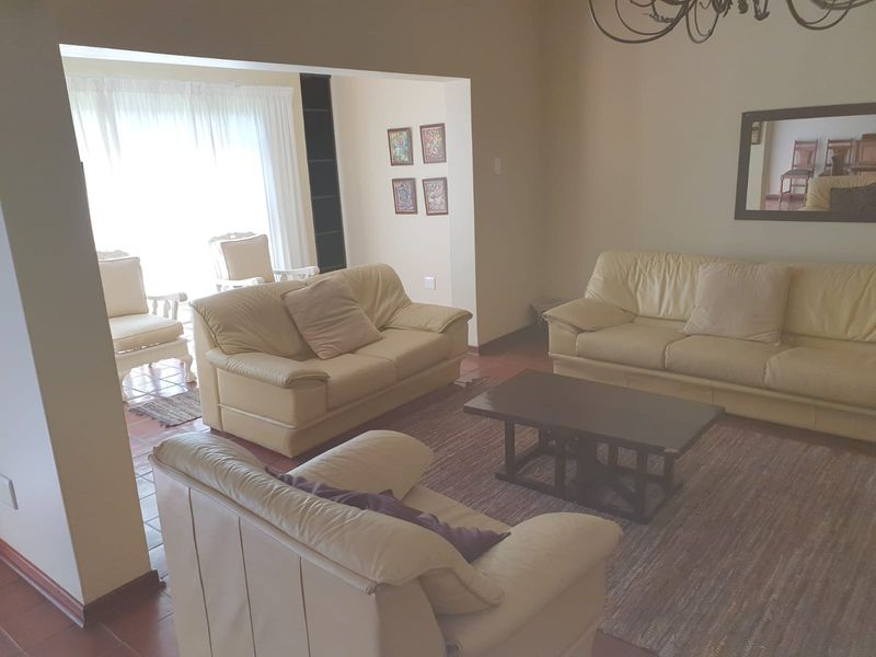 A spacious living room featuring tiled flooring and built-in shelving, with direct access to an adjacent sunlit area.