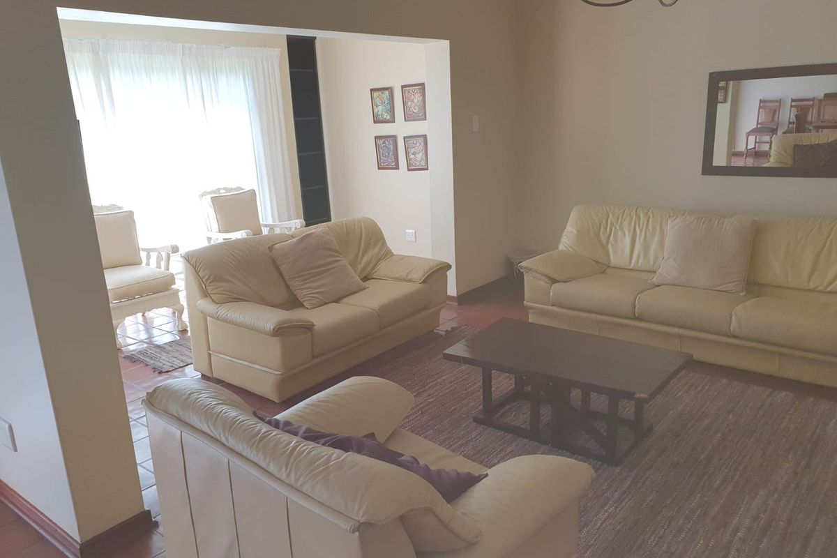 A spacious living room featuring tiled flooring and built-in shelving, with direct access to an adjacent sunlit area.
