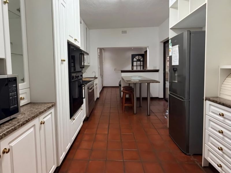 A functional kitchen featuring white cabinetry, granite countertops, built-in oven, and terracotta tile flooring, leading into an adjacent dining or living area.