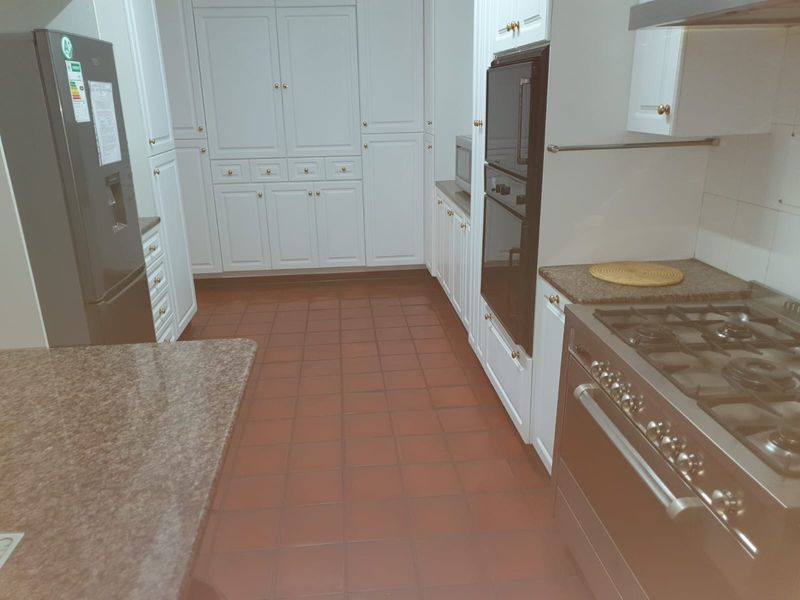 A functional kitchen featuring white cabinetry, granite countertops, a gas stove, and a built-in oven, finished with durable terracotta-style floor tiles.