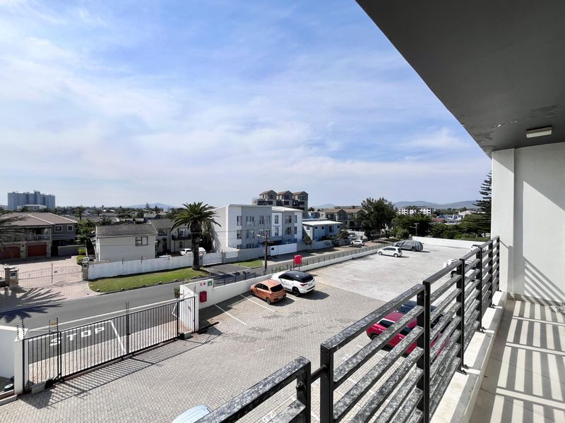 A balcony with a metal balustrade offering an elevated view over the complex parking area and surrounding neighborhood.
