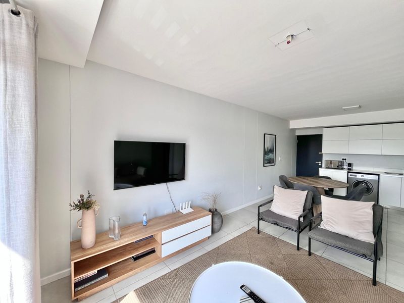 An open-plan living and kitchen area featuring tiled flooring, modern cabinetry, and an integrated washing machine in a bright, well-maintained space.