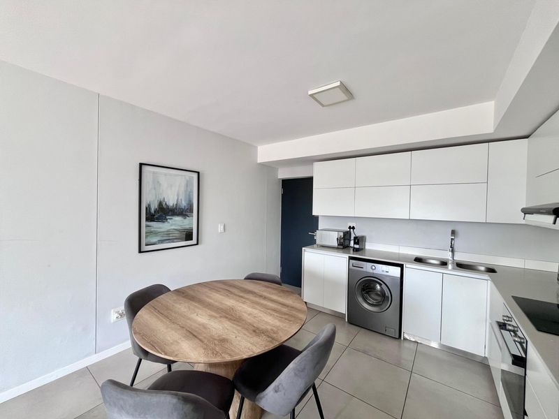 Modern open-plan kitchen and dining area featuring sleek white cabinetry, integrated appliances, and neutral tiled flooring.