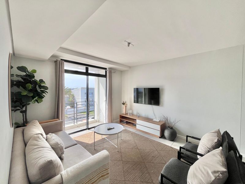 A bright and modern living room featuring tiled flooring, a recessed ceiling, and a large sliding glass door providing access to a private balcony.