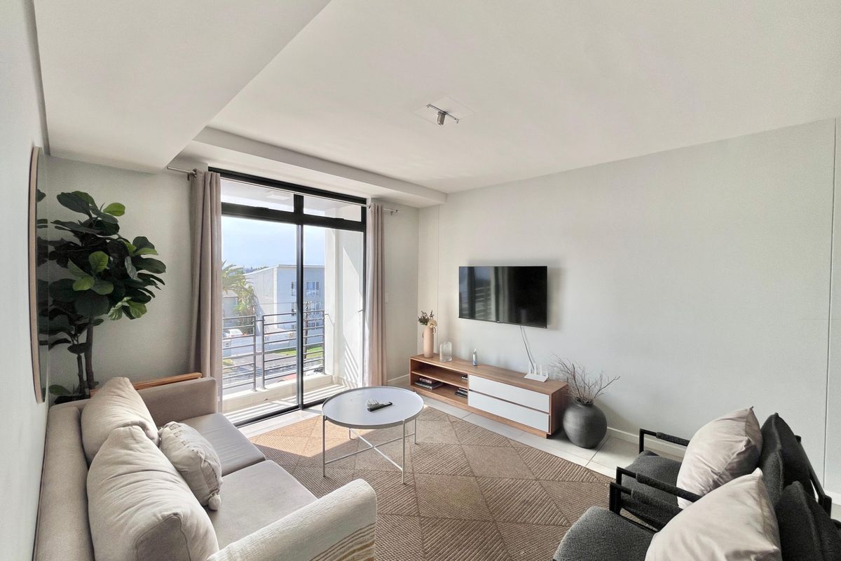 A bright and modern living room featuring tiled flooring, a recessed ceiling, and a large sliding glass door providing access to a private balcony.