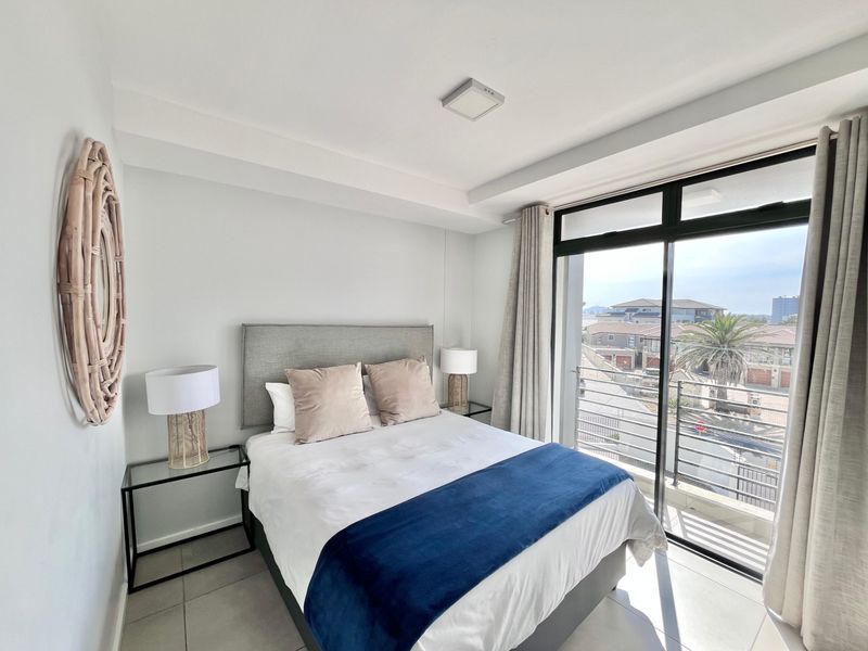 A bright bedroom featuring tiled floors and a large sliding glass door that opens onto a balcony with neighbourhood views.