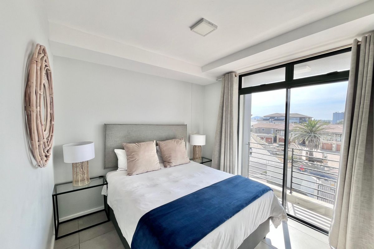 A bright bedroom featuring tiled floors and a large sliding glass door that opens onto a balcony with neighbourhood views.