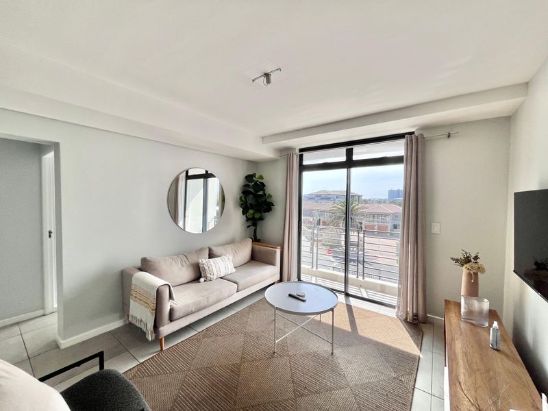 A bright and modern living room featuring tiled flooring and large sliding glass doors that open onto a balcony with neighborhood views.