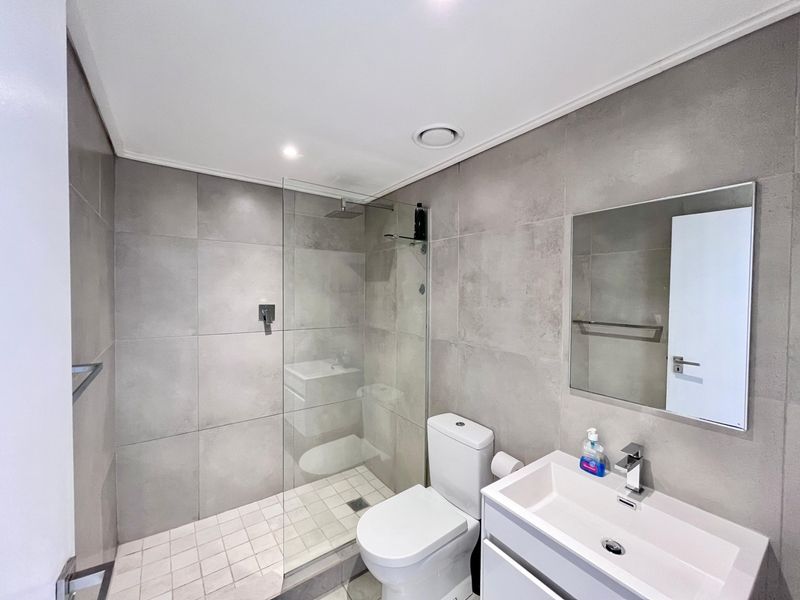 Modern bathroom featuring a walk-in shower with glass screen, contemporary vanity with basin, and neutral large-format wall tiles.