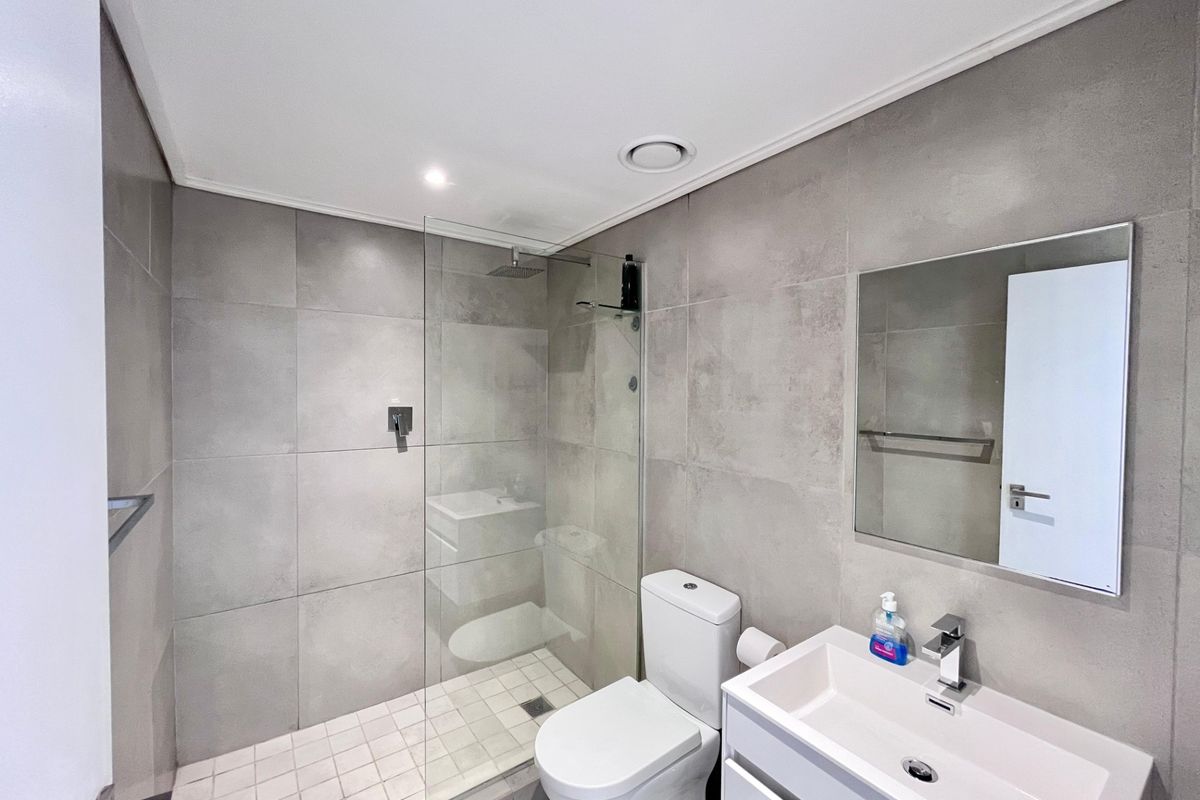Modern bathroom featuring a walk-in shower with glass screen, contemporary vanity with basin, and neutral large-format wall tiles.
