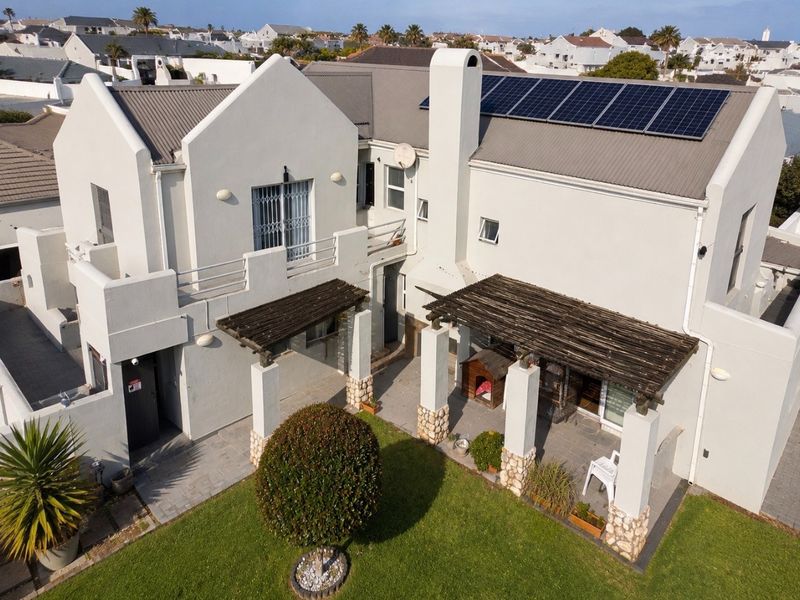 Aerial view of the rear elevation featuring a tiled patio with timber pergolas, stone-clad pillars, a balcony, and roof-mounted solar panels.