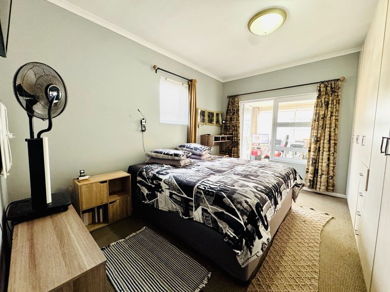A functional bedroom featuring built-in cupboards, neutral wall tones, and a sliding door providing access to an outdoor area.