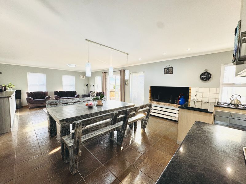 Spacious open-plan living and dining area featuring tiled floors, a built-in fireplace, and a functional kitchen with granite countertops and modern lighting.
