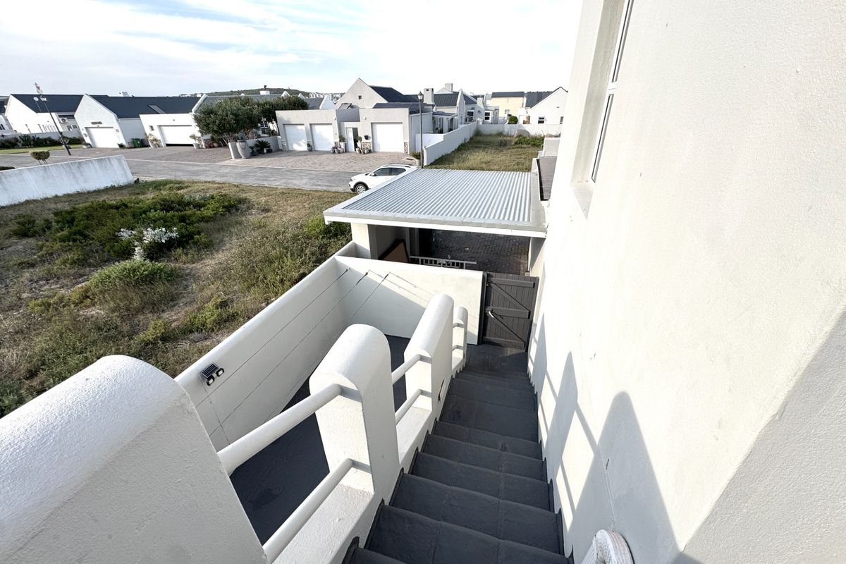 An elevated view of the rear exterior featuring an external staircase leading down to a paved area with a metal roof carport and boundary wall.