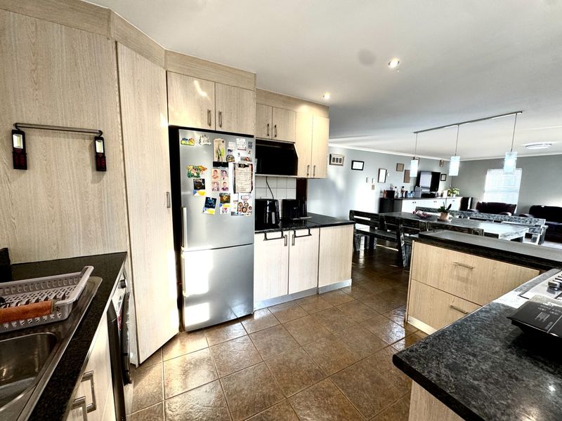 Open-plan kitchen and living area featuring light wood-finish cabinetry, dark countertops, and tiled flooring with integrated lighting fixtures.