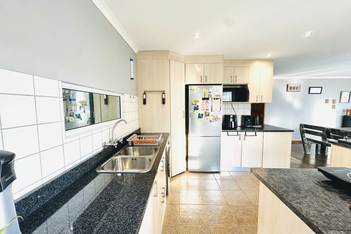 A functional kitchen featuring granite countertops, double stainless steel sink, ample built-in cabinetry, and tiled splashbacks with recessed lighting.