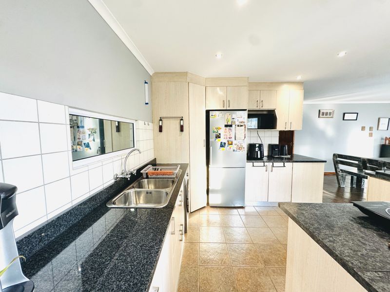 A functional kitchen featuring granite countertops, double stainless steel sink, ample built-in cabinetry, and tiled splashbacks with recessed lighting.