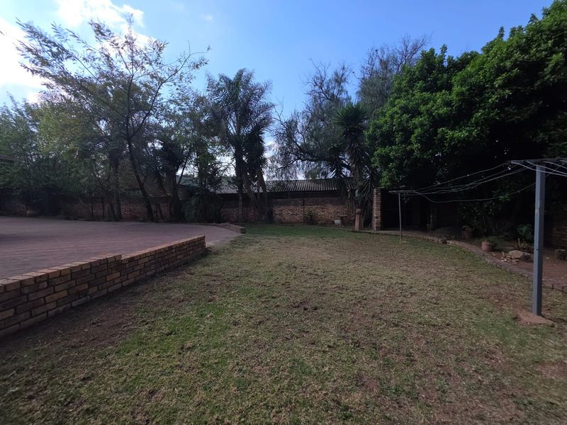 A spacious rear garden featuring a paved patio area, established trees, and a brick boundary wall.