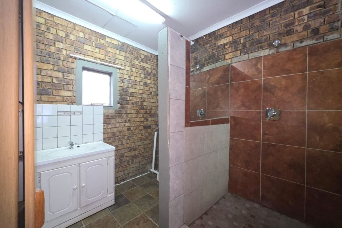 Bathroom featuring a vanity basin and a walk-in shower with exposed brick walls and tiled flooring, requiring cosmetic updates to modernize the space.