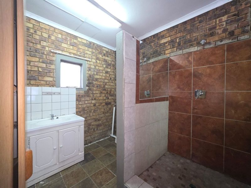 Bathroom featuring a vanity basin and a walk-in shower with exposed brick walls and tiled flooring, requiring cosmetic updates to modernize the space.