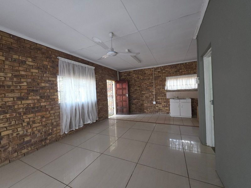 Open-plan living area featuring exposed brick walls, tiled flooring, a ceiling fan, and a basic kitchenette corner with a sink.