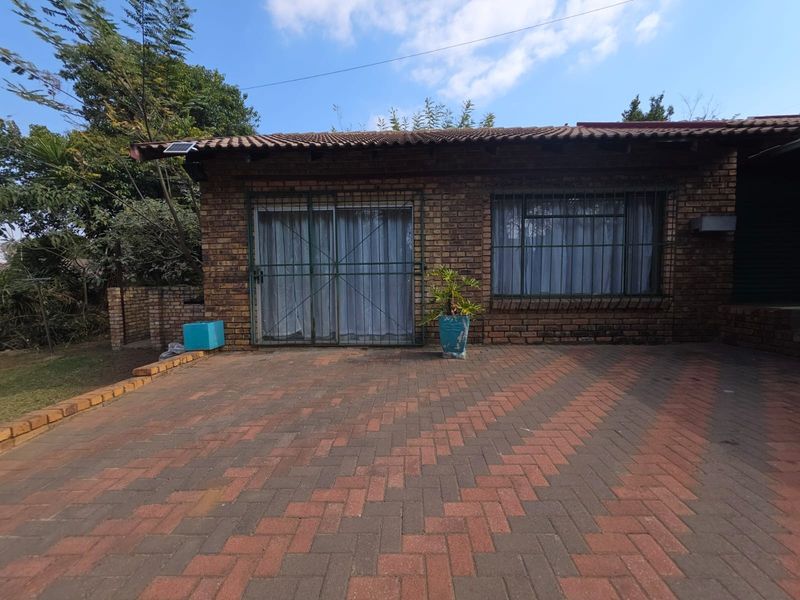 Rear exterior view of a face brick apartment featuring a paved patio area, sliding door access, and security fixtures.