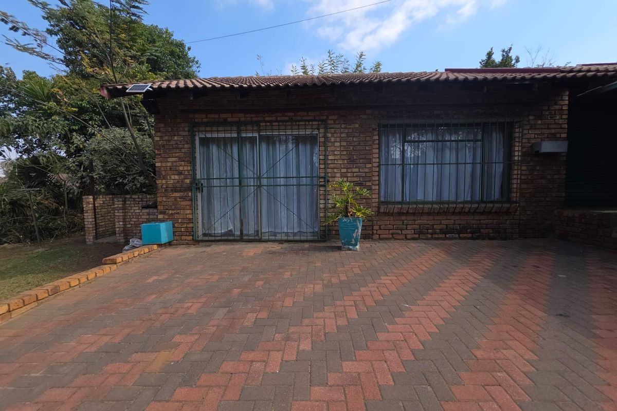 Rear exterior view of a face brick apartment featuring a paved patio area, sliding door access, and security fixtures.