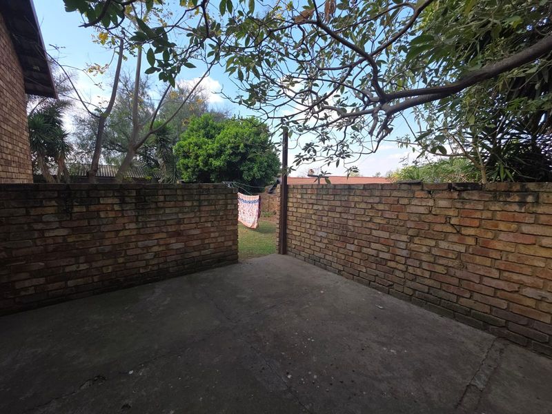 A private rear courtyard featuring a concrete patio area enclosed by brick boundary walls, offering potential for outdoor landscaping and improvement.