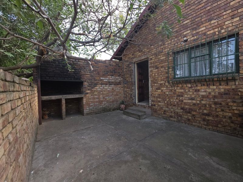 Rear exterior area featuring a built-in brick braai, concrete patio, and direct access to the apartment through a security door.
