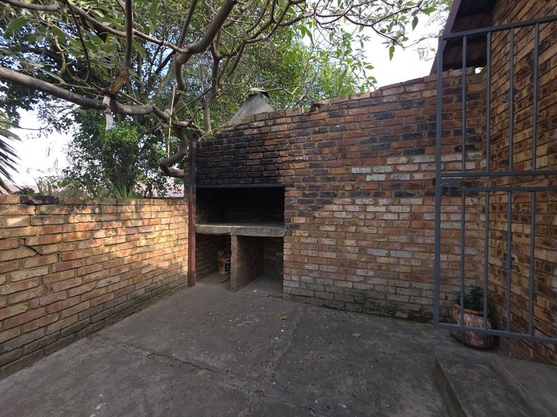 An outdoor rear patio area featuring a built-in brick braai, concrete flooring, and enclosed by brick boundary walls.