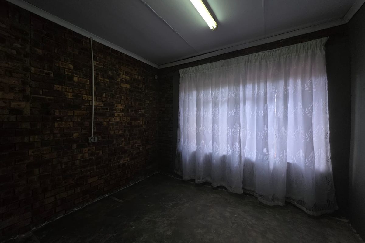 An empty bedroom featuring an exposed brick feature wall, concrete flooring, and a fluorescent ceiling light fixture.