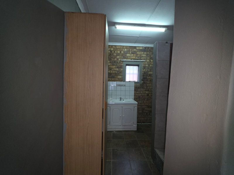 A functional bathroom space featuring a vanity basin, tiled splashback, and exposed brick wall finish, presenting an opportunity for modernization and cosmetic updates.