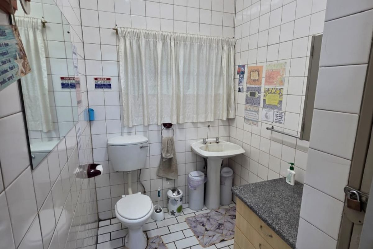 A functional commercial bathroom featuring a pedestal basin, toilet, and vanity cabinet with granite countertop, finished with full-height ceramic wall tiling.