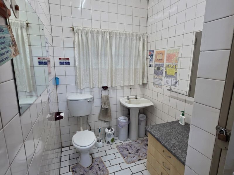 A functional commercial bathroom featuring a pedestal basin, toilet, and vanity cabinet with granite countertop, finished with full-height ceramic wall tiling.