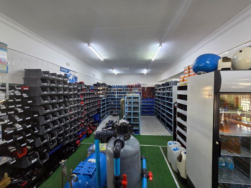 Commercial utility space featuring extensive built-in shelving for inventory storage, tiled wall finishes, and integrated plumbing infrastructure.