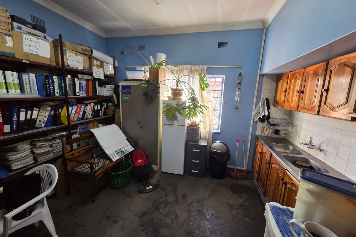A functional kitchen area featuring wooden cabinetry, a double bowl stainless steel sink, and tiled splashbacks, currently utilized for storage and workspace.