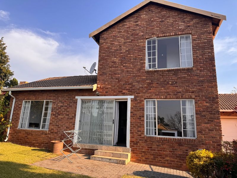Rear view of a double-story face brick townhouse featuring a paved patio area, sliding glass doors with security gates, and large windows.