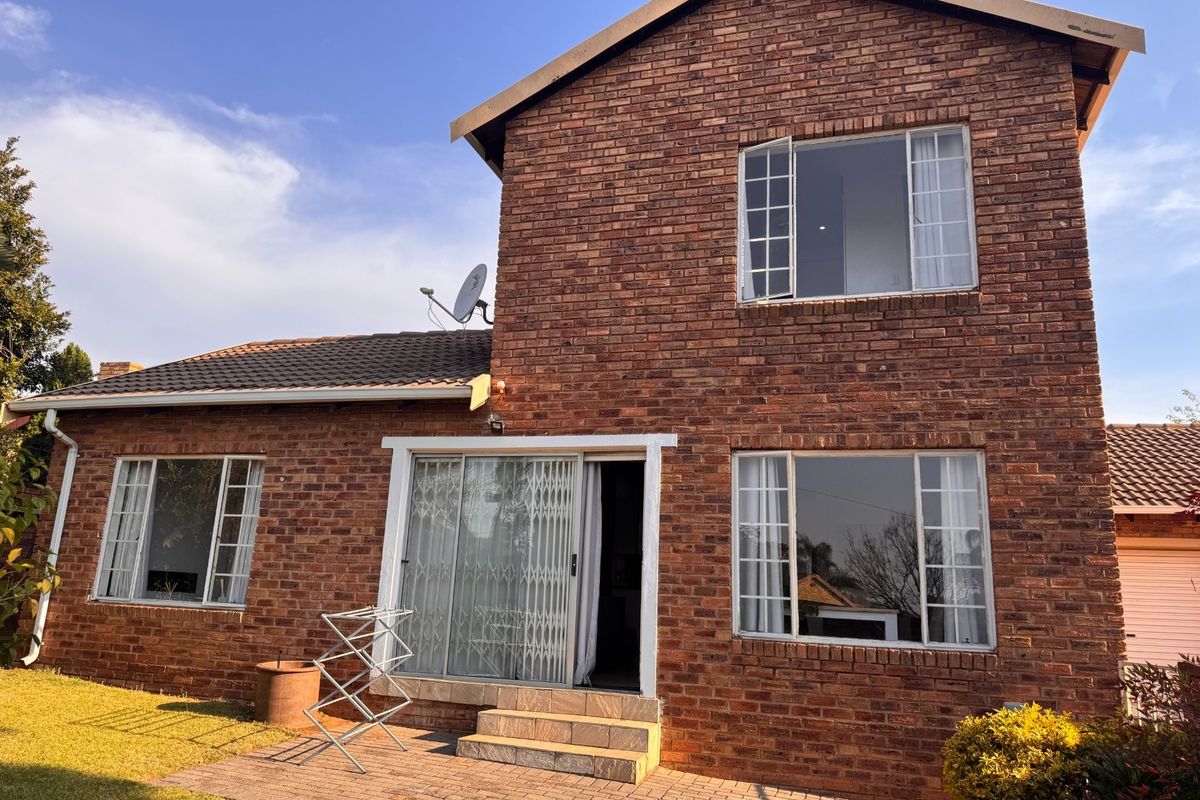 Rear view of a double-story face brick townhouse featuring a paved patio area, sliding glass doors with security gates, and large windows.