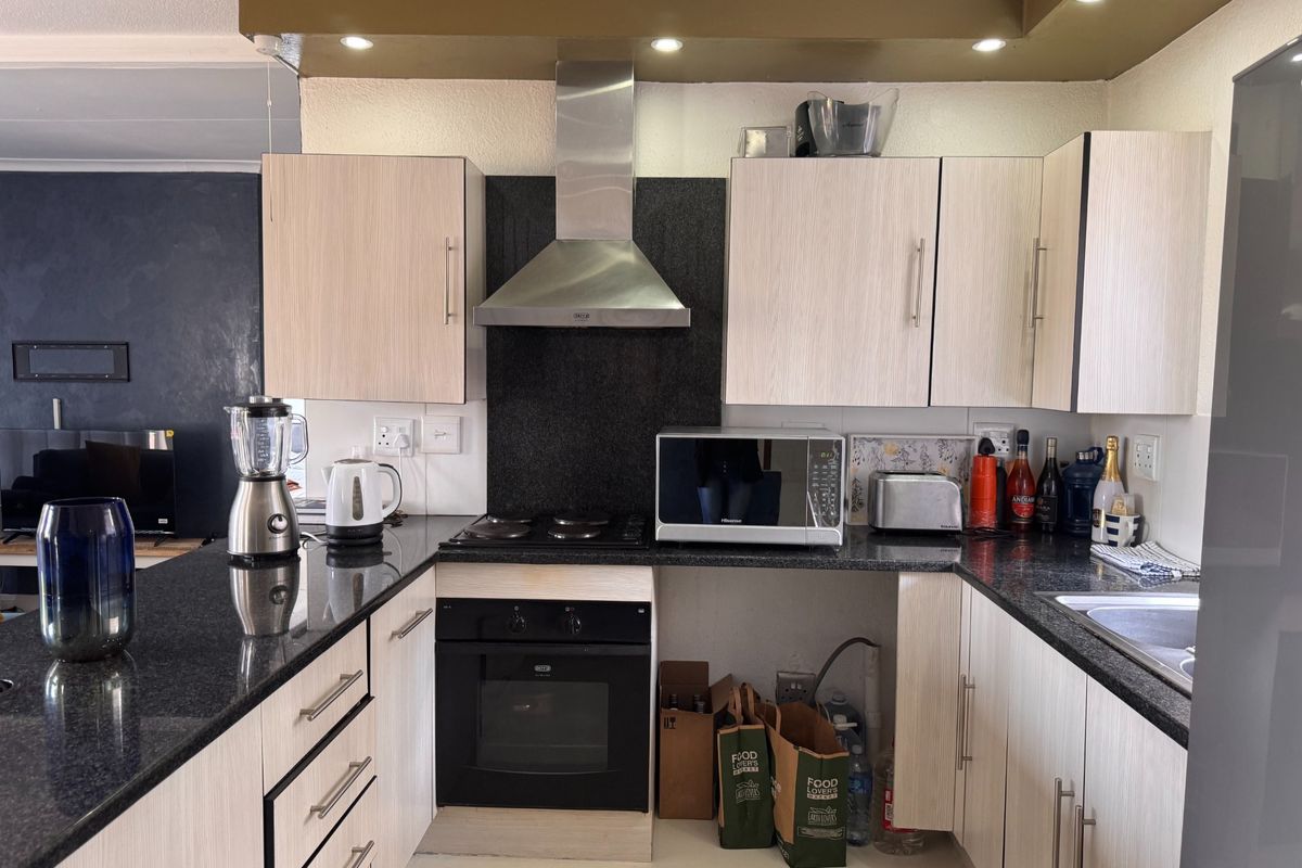 A functional kitchen featuring granite countertops, built-in oven, stainless steel extractor fan, and light-toned cabinetry with recessed lighting.
