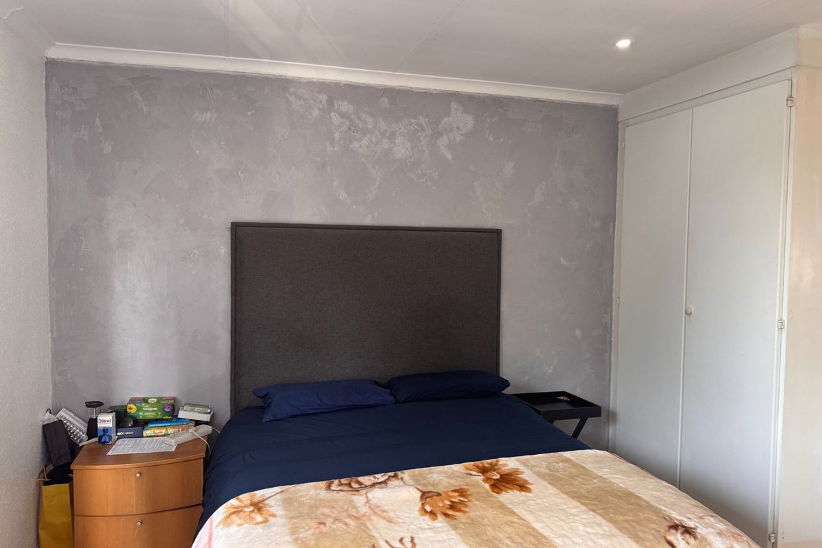 A bedroom featuring built-in cupboards, recessed downlighting, and a textured feature wall.