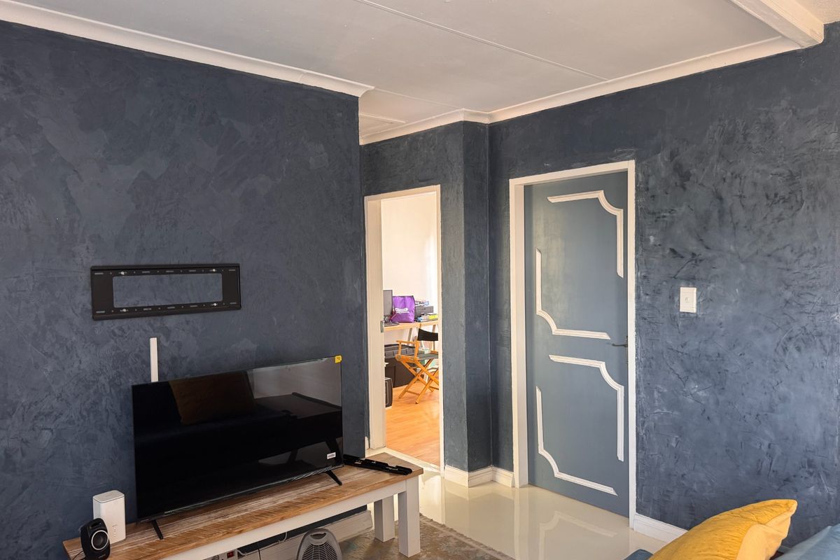 A living room featuring dark textured walls, tiled flooring, and a coved ceiling, with a doorway leading to an adjacent room.