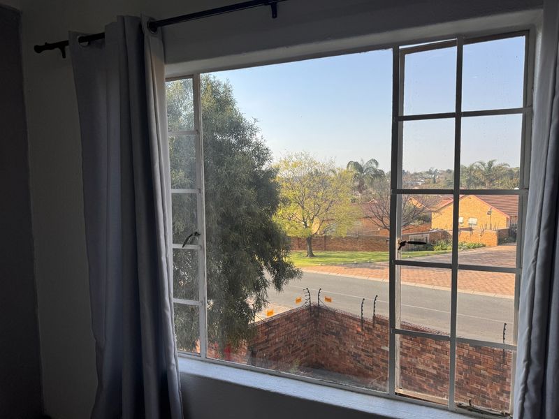 A view from a window looking out over a residential street, featuring a brick boundary wall with electric fencing and mature trees.