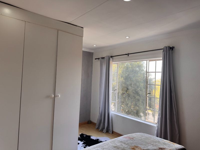 A bright bedroom featuring built-in cupboards, recessed downlighting, and laminated flooring, offering a clean and functional living space.
